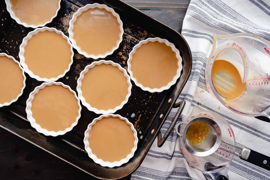 Strained and filled custard in shallow ramekins inside a large roasting pan