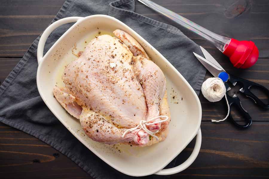 Stuffed, tied, and seasoned chicken in a ceramic baking dish